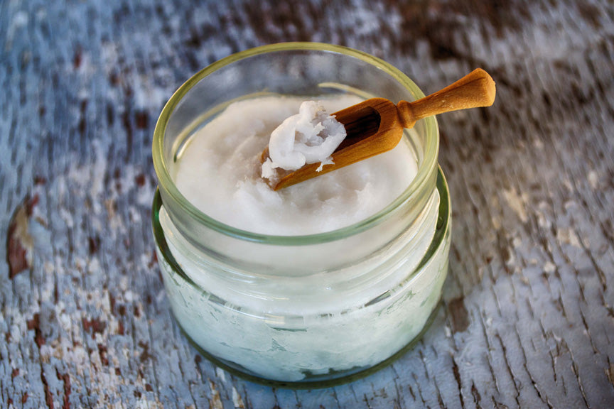 A glass jar filled with solidified coconut oil, with a small wooden spoon scooping some out, placed on a rustic wooden surface.