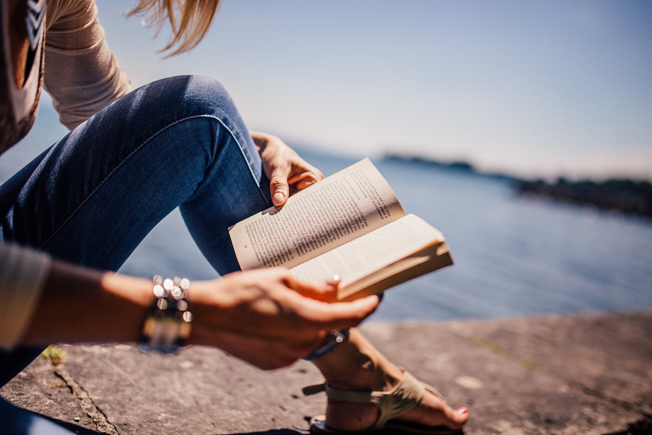 person reading a book by lake water