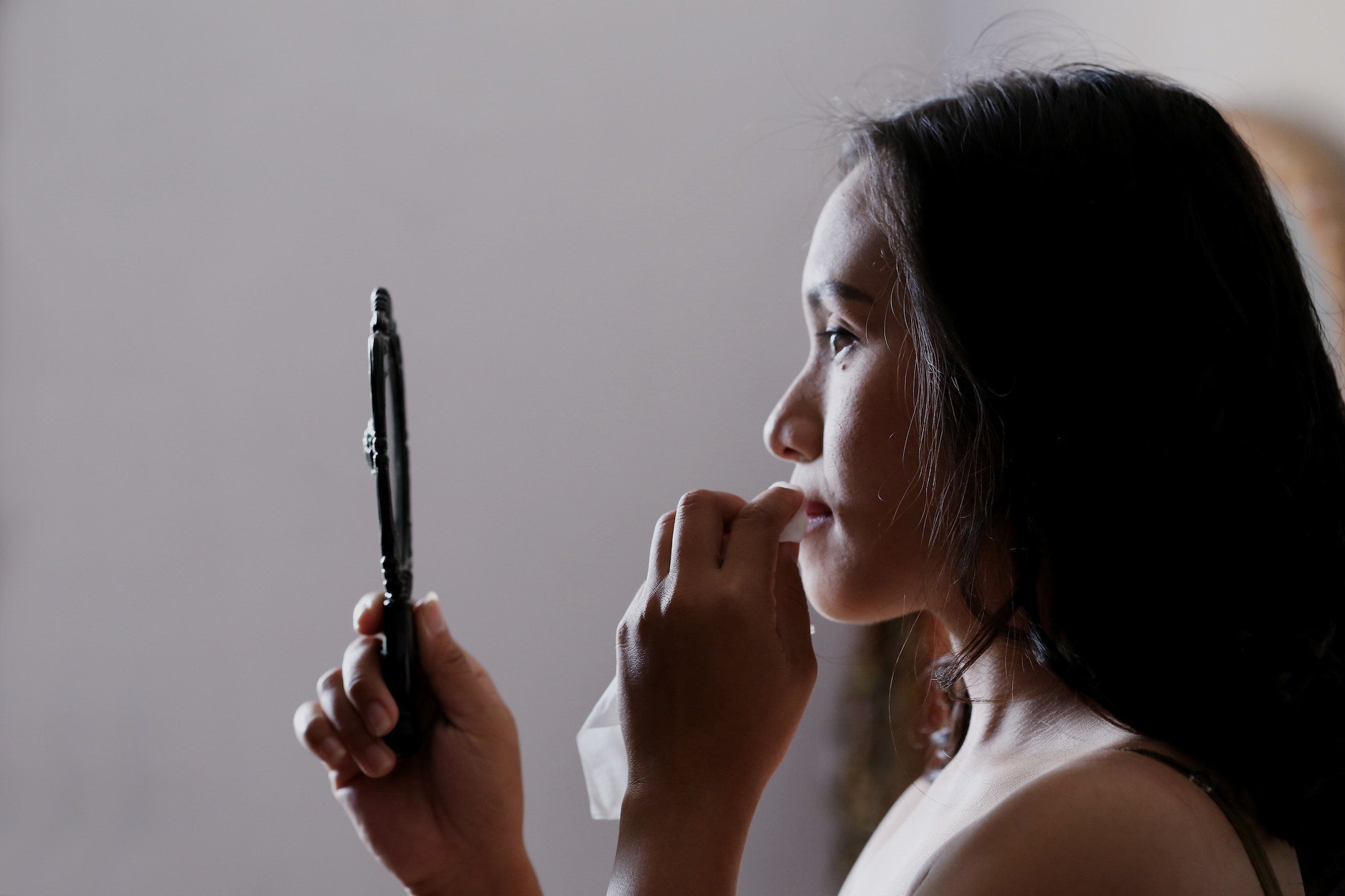 woman looking in mirror removing lipstick with tissue