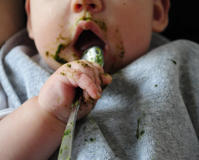 baby eating something green with spoon