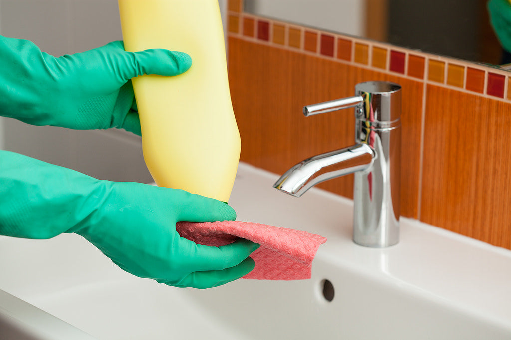 A man cleaning a bathroom using a rag and a detergent