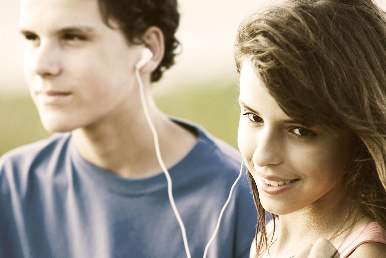 Teens sharing earphones, listening to music outdoor.