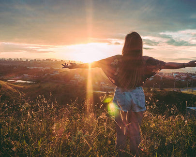 Woman Stands on Mountain over Field Under Cloudy Sky at Sunrise