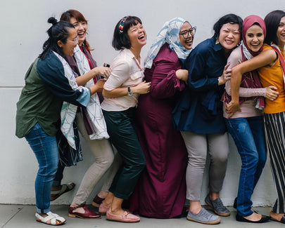 seven women standing against a white wall laughing